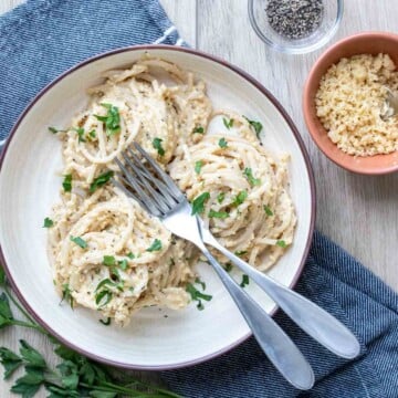 A cream colored plate with three twirled piles of spaghetti in a creamy sauce