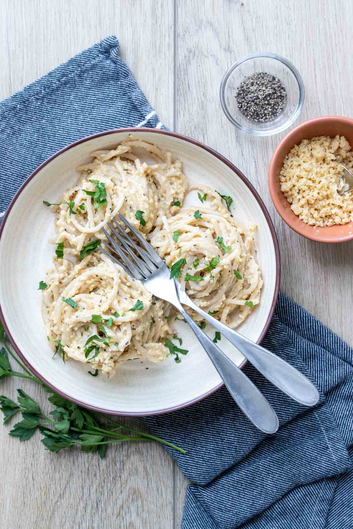 A cream colored plate with three twirled piles of spaghetti in a creamy sauce