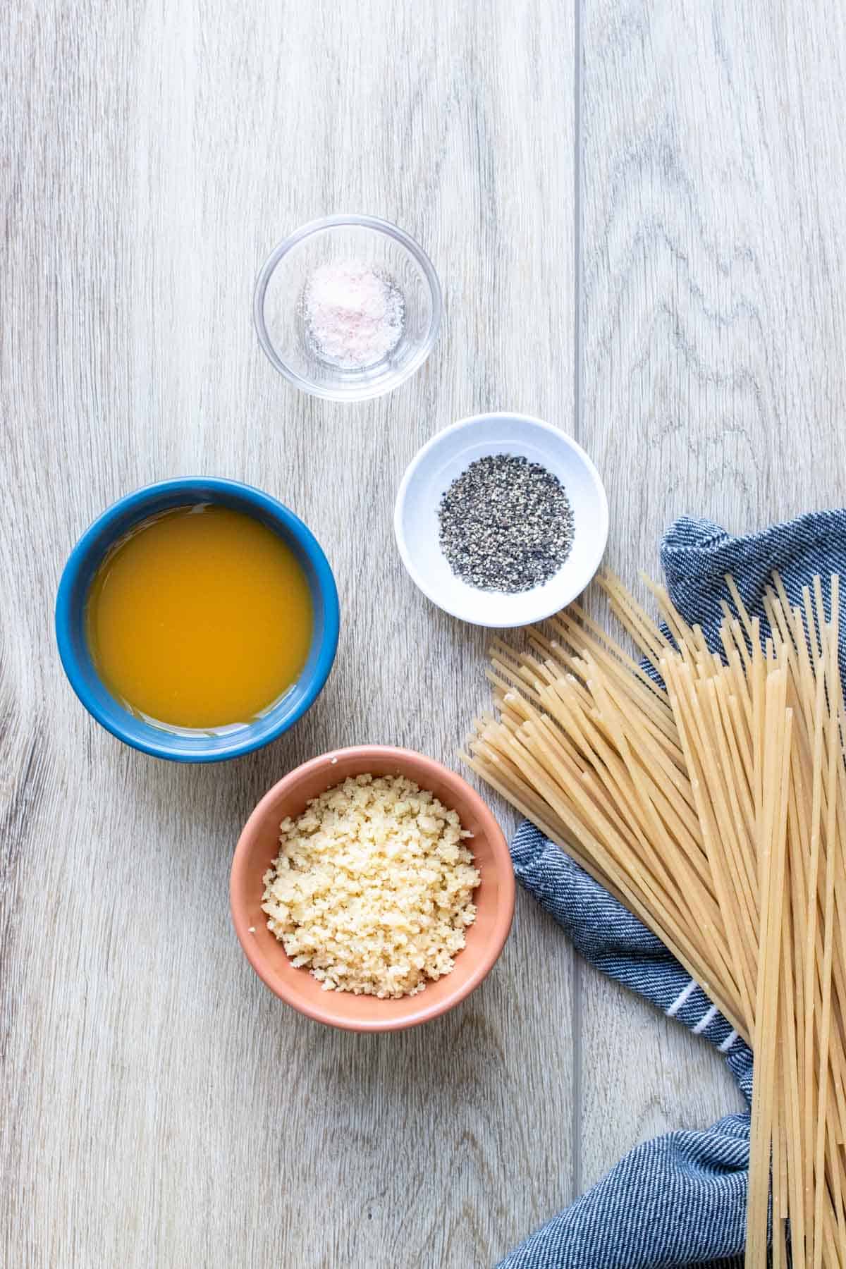 Dry spaghetti, broth, parmesan, salt and pepper on a light wooden surface