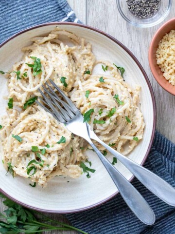 Cream plate with three piles of spaghetti in a creamy like sauce topped with parsley