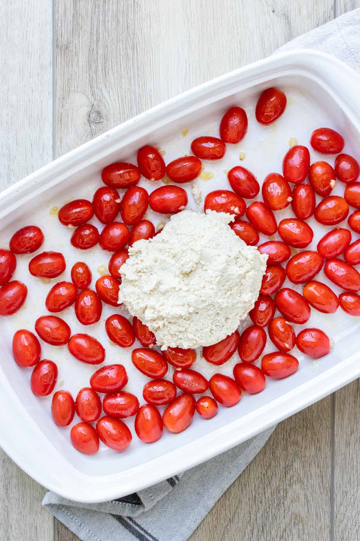 Pile of feta over grape tomatoes in a white baking dish