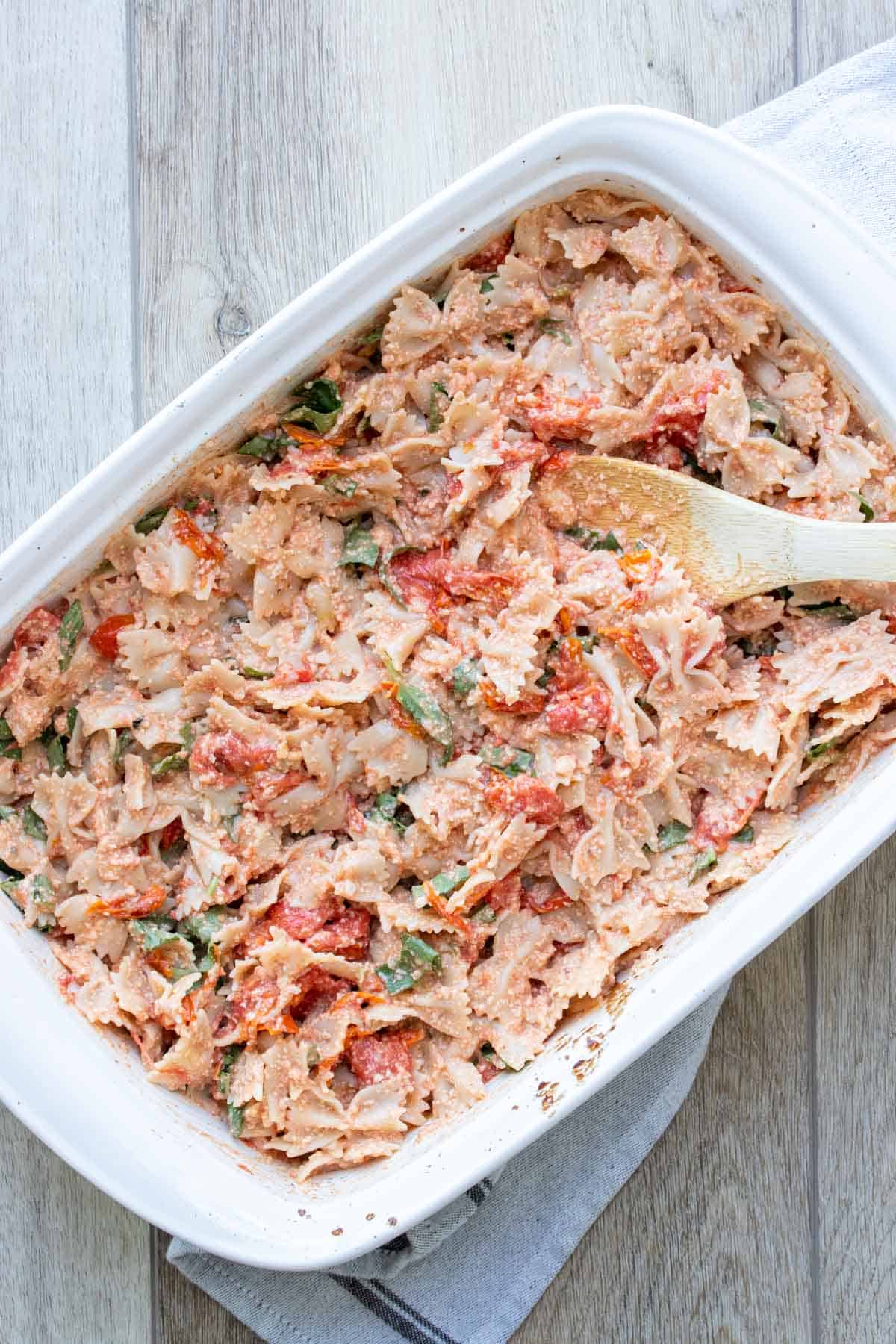 White baking dish with a wooden spoon and filled with a tomato and feta pasta