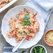 A white bowl with feta and tomato pasta topped with basil next to a baking dish of it