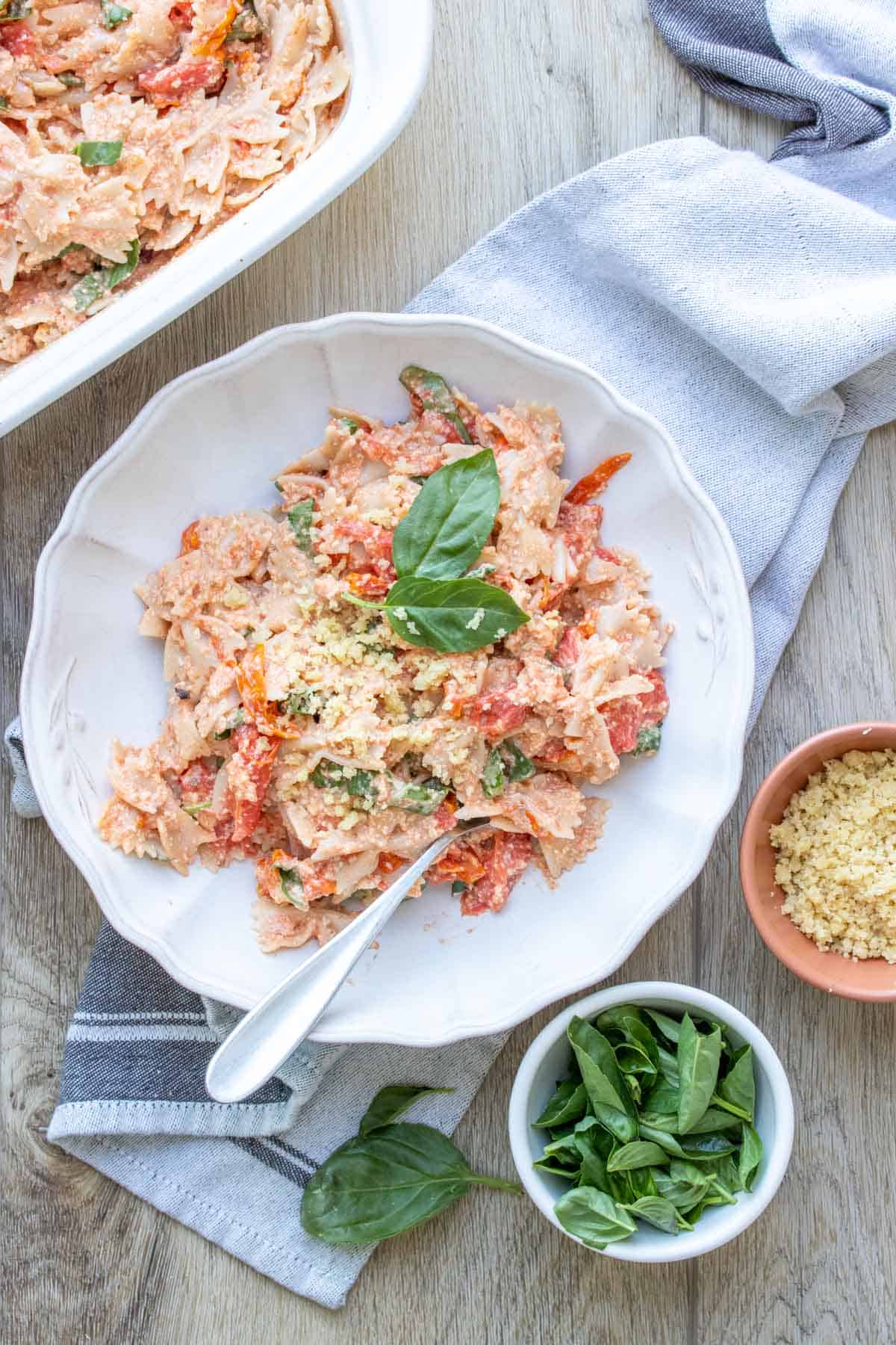 A white bowl with feta and tomato pasta topped with basil next to a baking dish of it