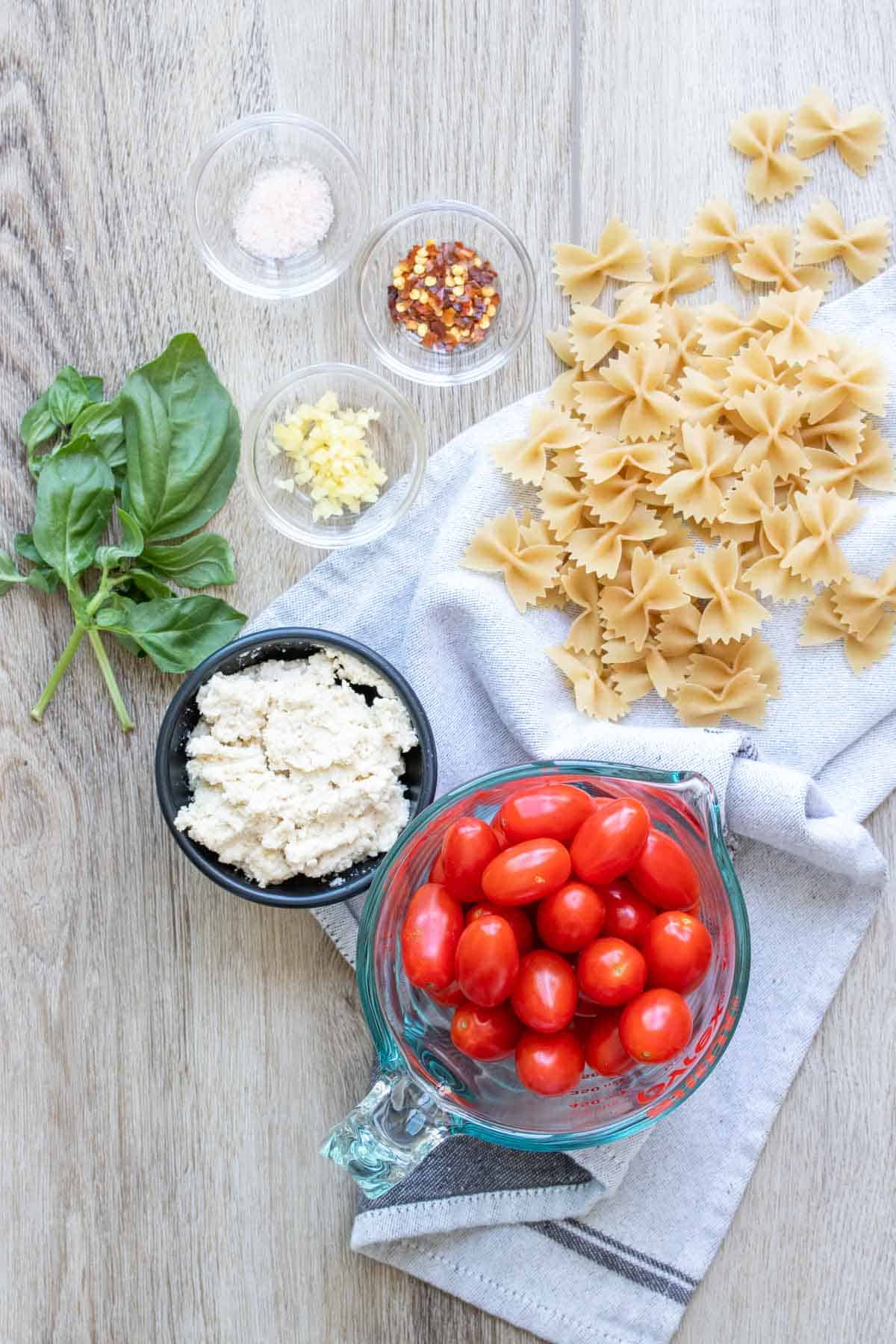 Grape tomatoes, feta, basil, spices and bow tie pasta on a light wooden surface