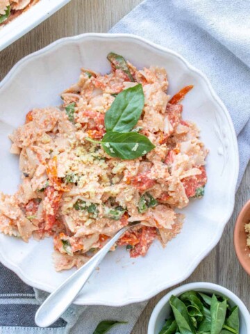 White bowl with pasta mixed with feta and tomatoes on a grey towel