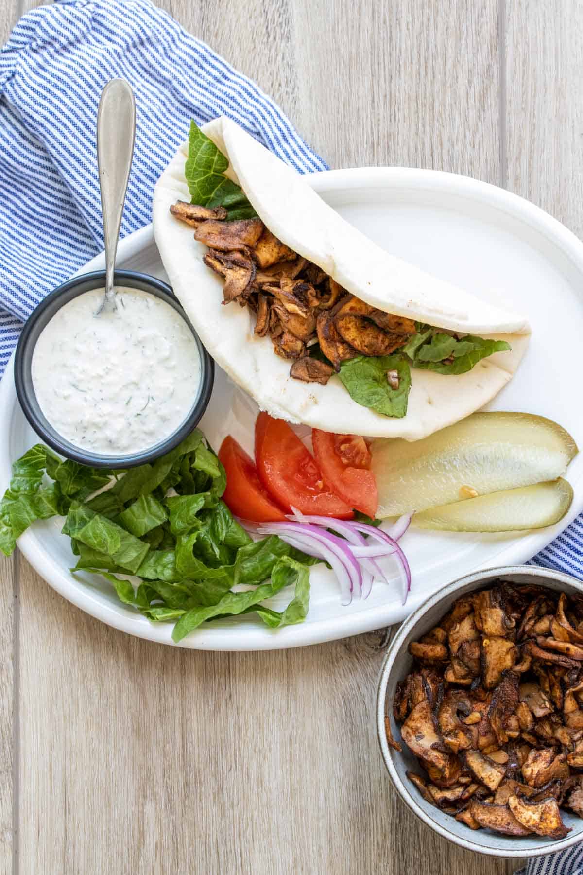 A pita bread being stuffed with portobello slices on a platter next to toppings.