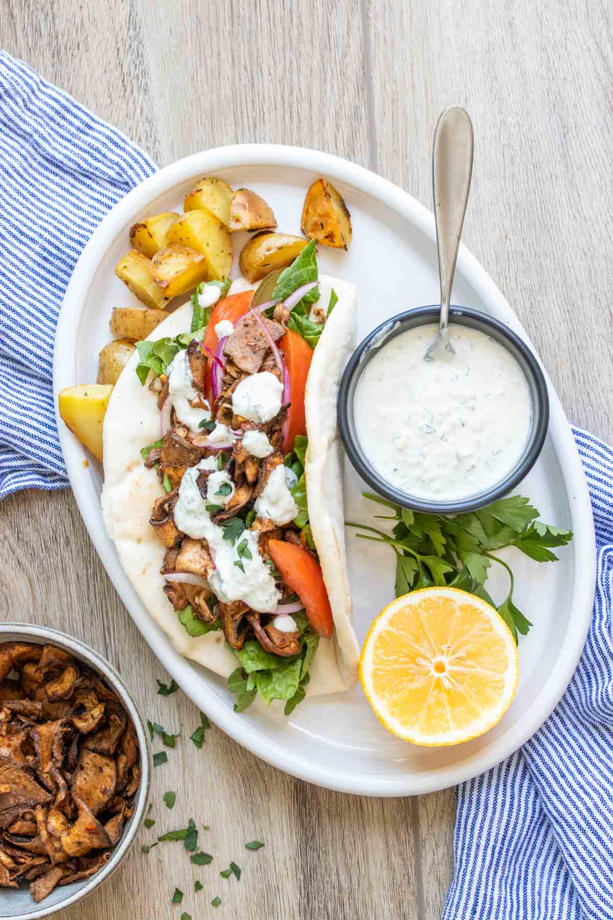 A pita bread filled with sliced portobello and topped with lettuce, tomato, onion and white sauce on a white dish.