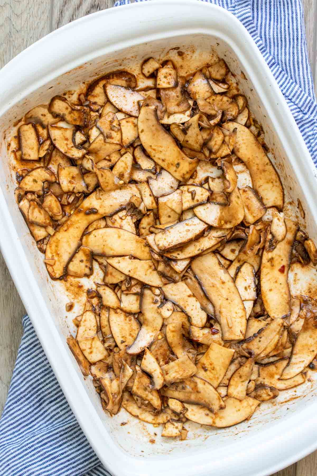 White baking dish with thinly sliced portobello covered in spices.