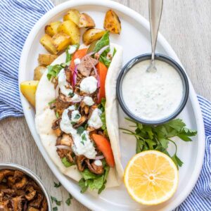 White plate with roasted potatoes and a sliced portobello pita sandwich with toppings.