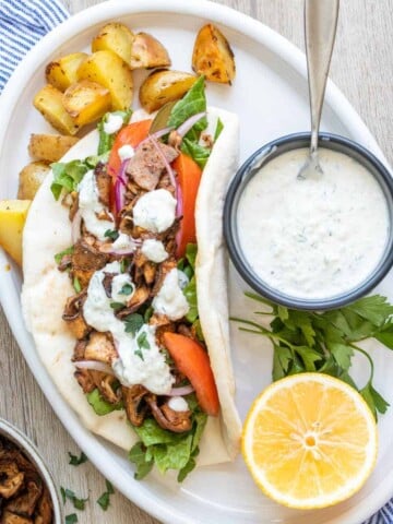 White plate with roasted potatoes and a sliced portobello pita sandwich with toppings.