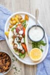 A pita stuffed with lettuce, baked sliced mushrooms, tomatoes, onions and a white sauce on a plate next to crisp potatoes and the sauce in a bowl.