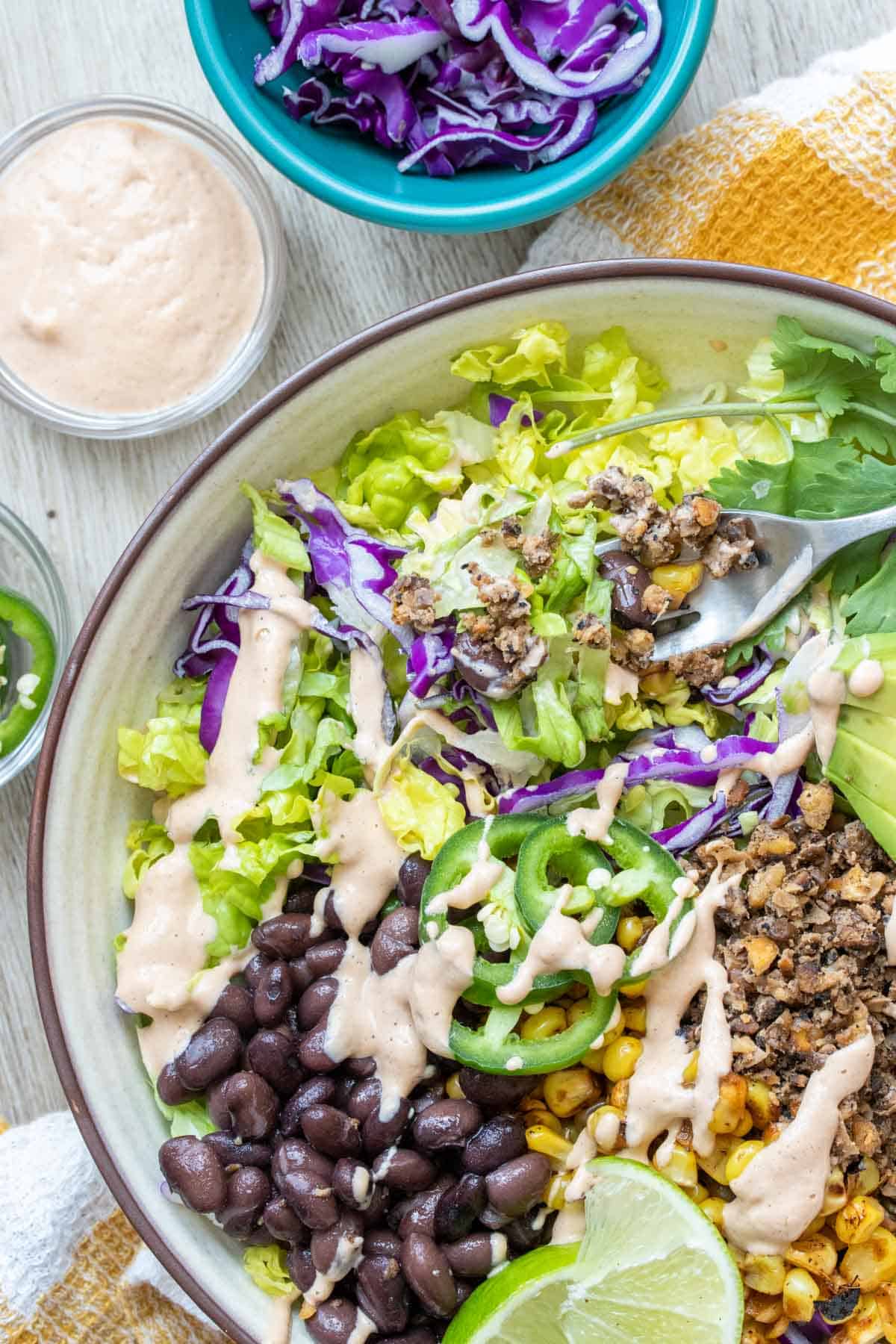 A fork getting a bite of taco salad from a white bowl with a brown rim