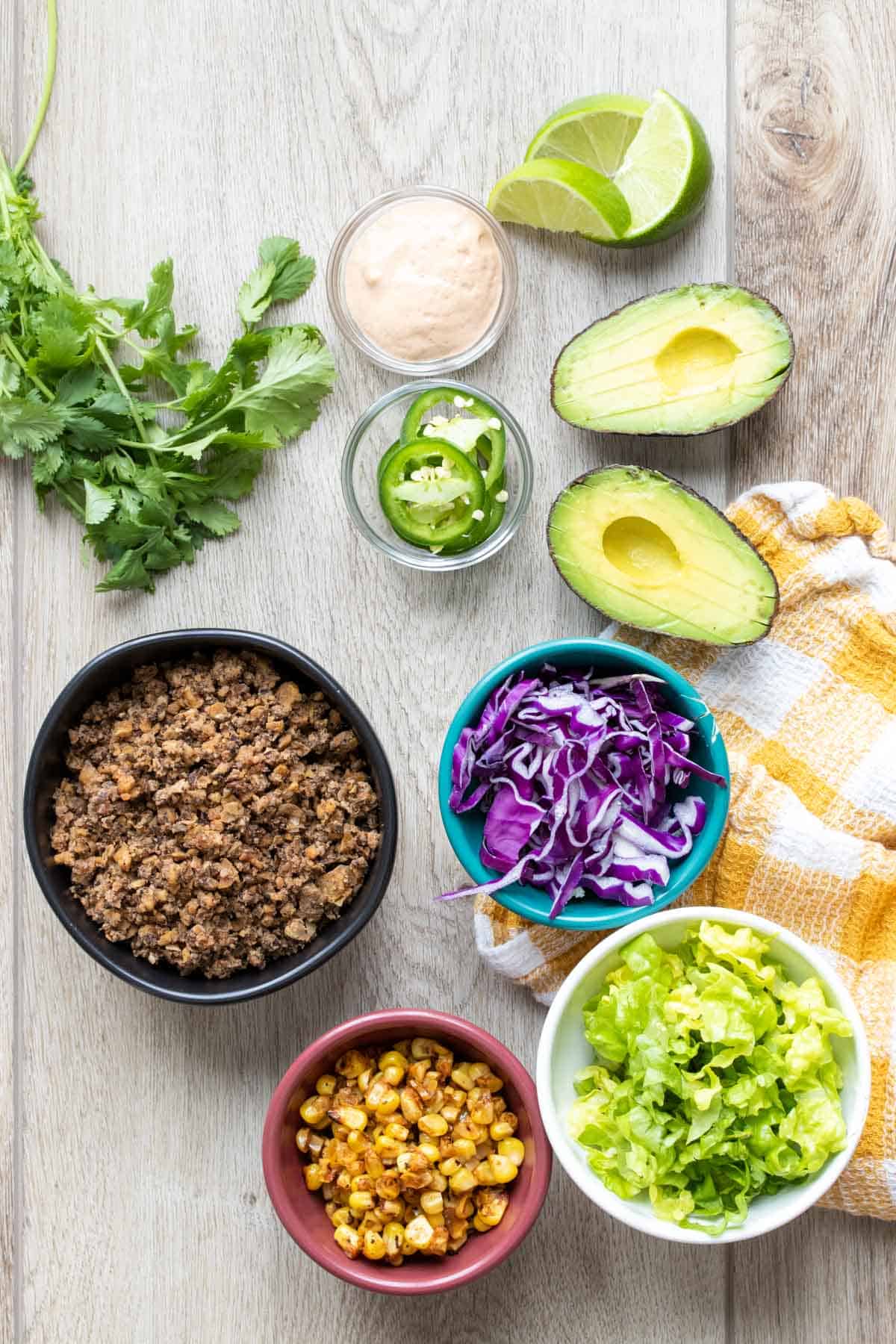 Ingredients for a taco salad on a wooden surface and in different colored bowls