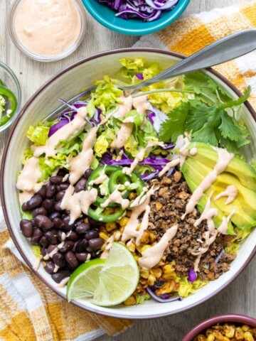 A taco salad loaded with toppings in a white bowl on a yellow checkered towel