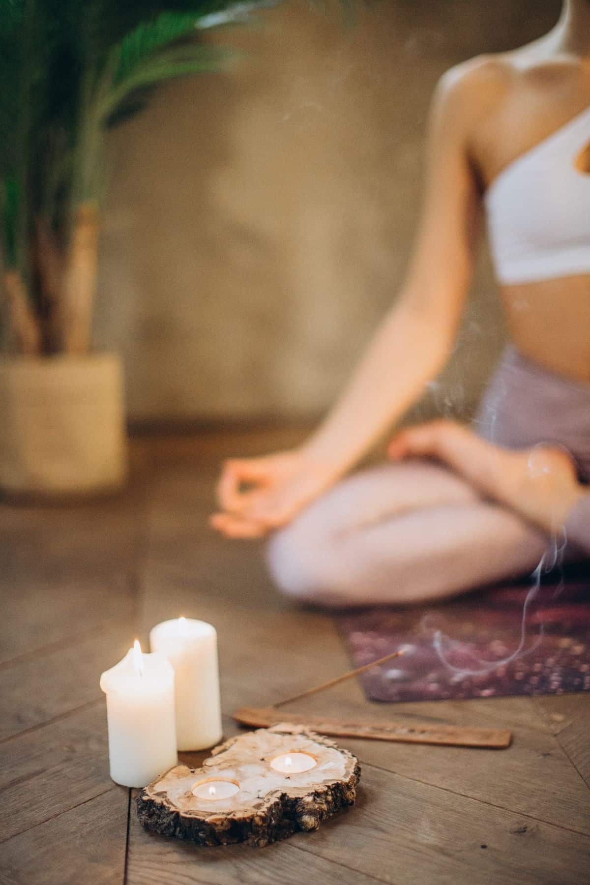 Part of a woman sitting in a yoga pose next to candles