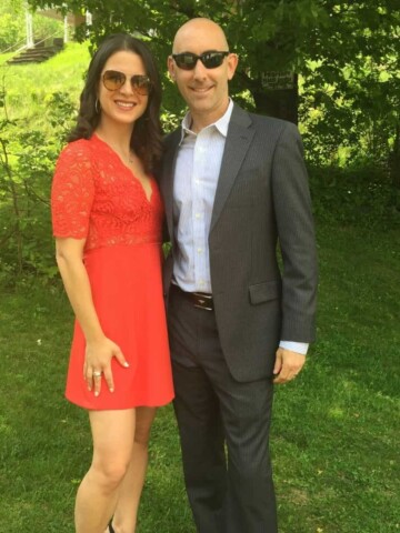 Man in a suit and a woman in a red dress smiling and standing next to each other