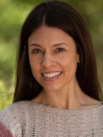 A woman with long brown hair wearing a pink sweater smiling