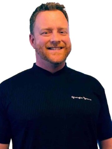 Man with blond short hair and beard in a black shirt smiling at the camera