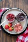 Top view of a plate with three jars on it filled with different flavors of jam