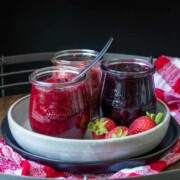 Front view of three jars filled with different jam flavors on a plate