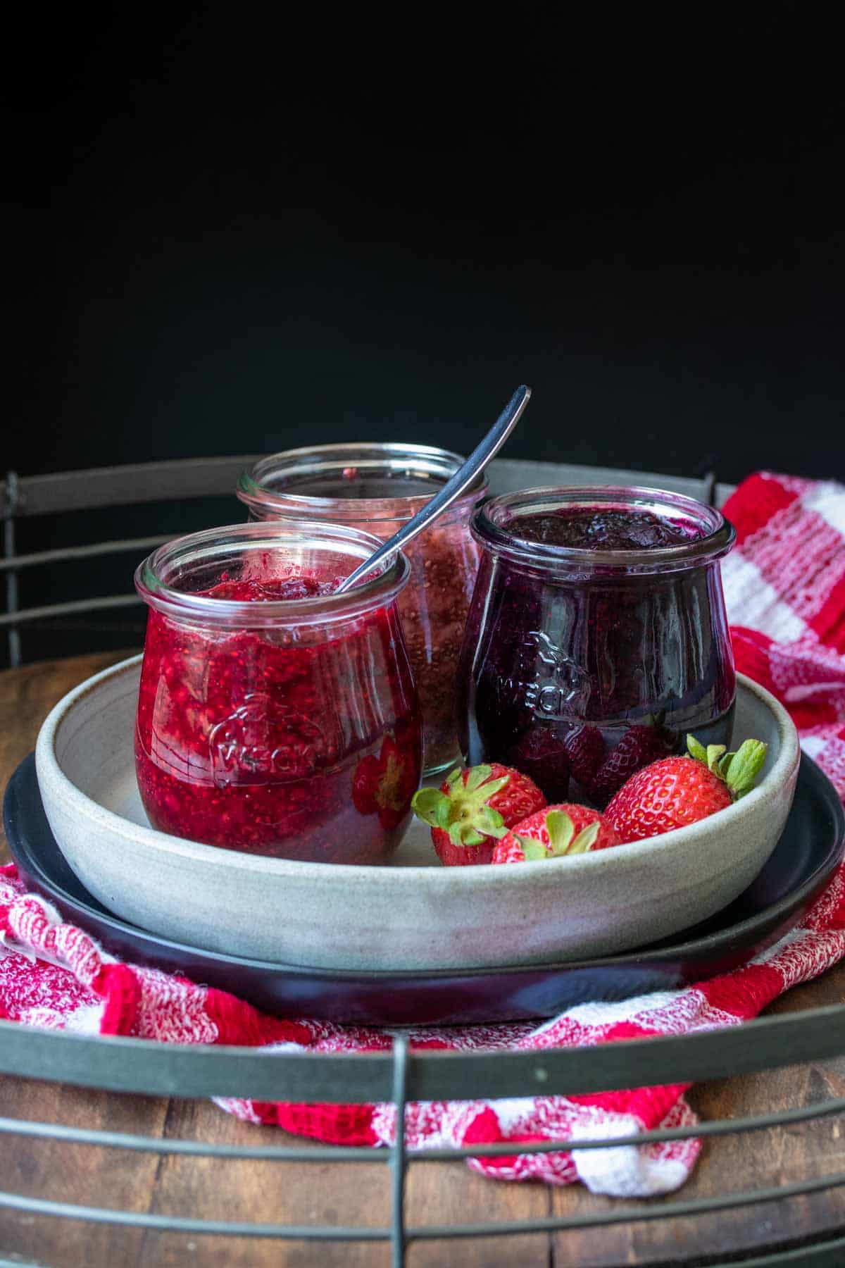 Front view of three jars filled with different jam flavors on a plate