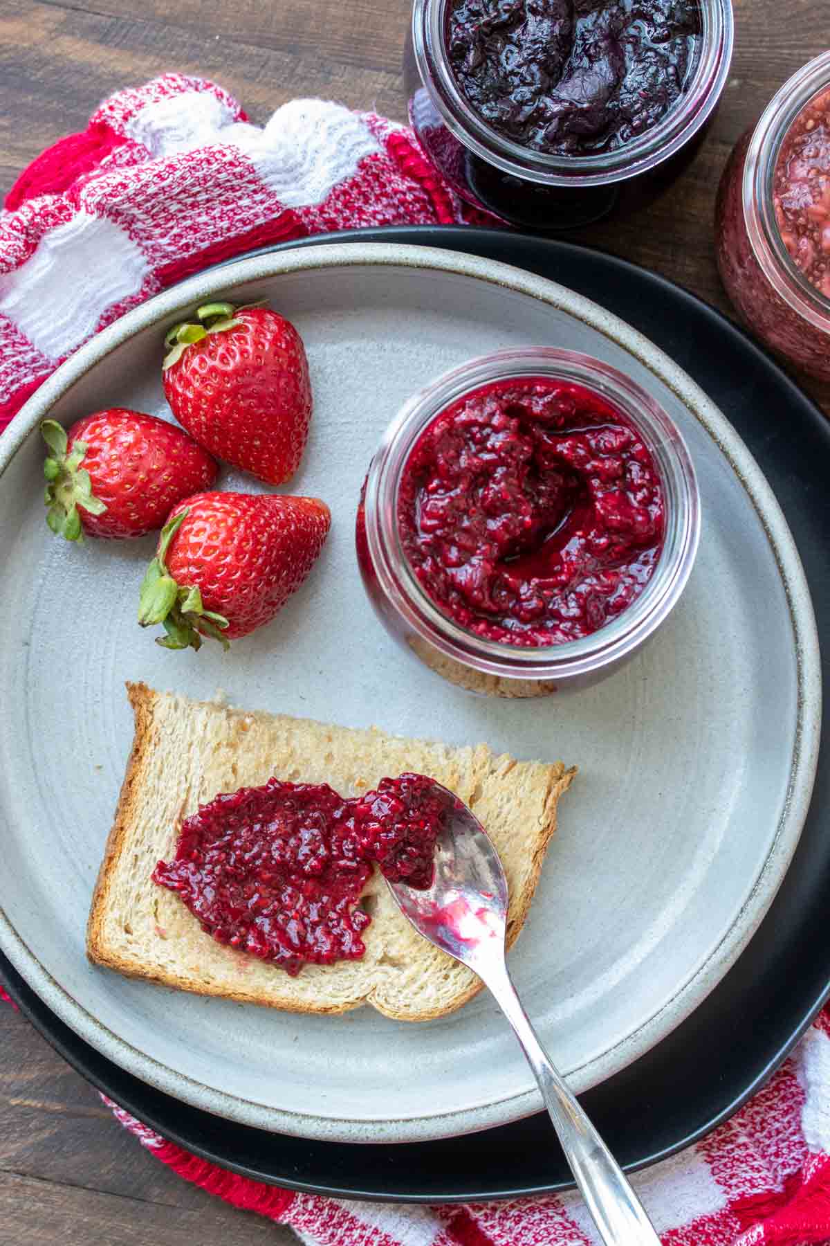 Top view of a knife spreading raspberry jam on a piece of toast on a plate