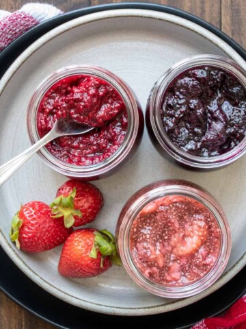 Three jars of different flavors of jam on a grey plate