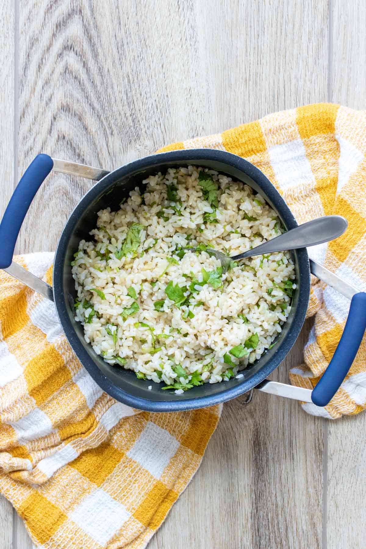 Pot with a spoon and cilantro lime rice inside on a wooden surface.