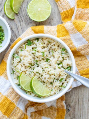 Bowl filled with chopped cilantro and rice mix and sliced limes.