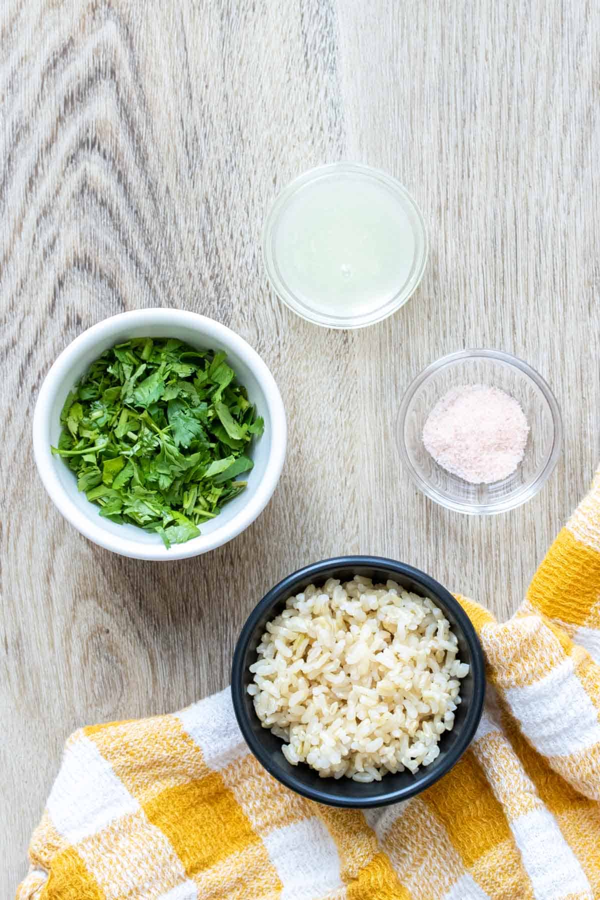 Bowls with cilantro, rice, lime juice and salt on a light wooden surface