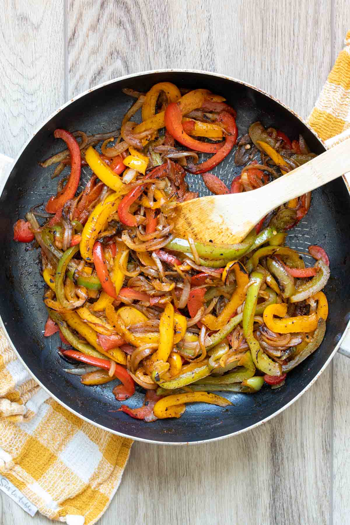 Sliced peppers and onion cooking in a pan on a checkered towel.