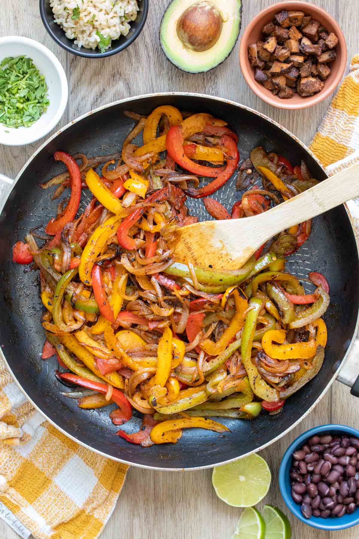 Wooden spoon mixing cooking peppers and onions in a pan