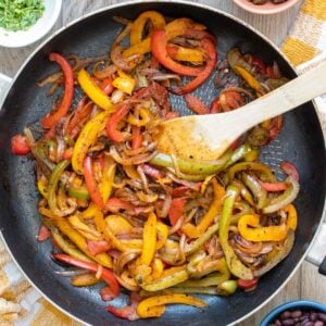 Wooden spoon mixing fajita veggies cooking in a pan.