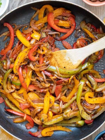 Wooden spoon mixing fajita veggies cooking in a pan.