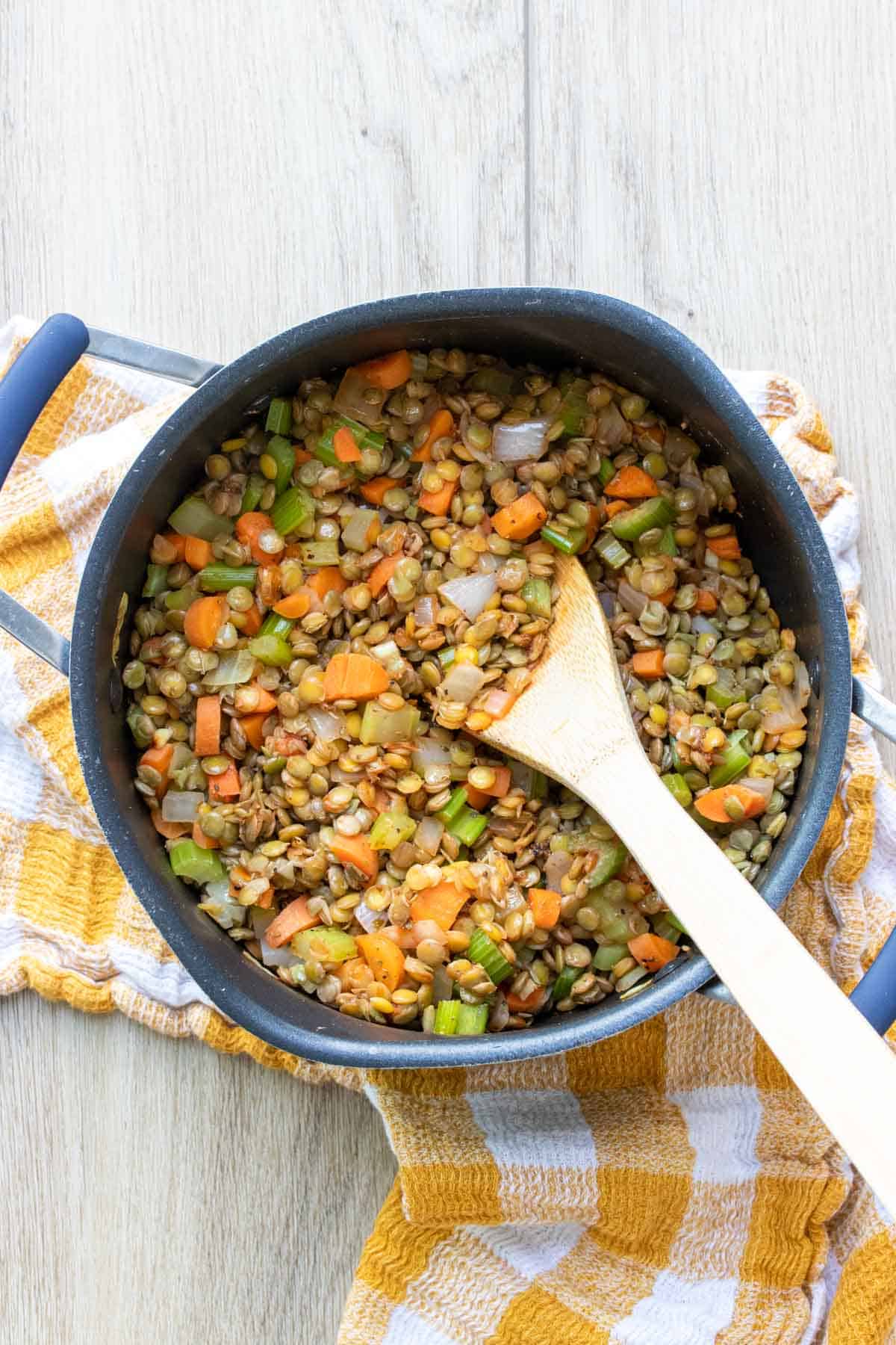 A big pot with lentils, carrots, celery and onion being sauteed