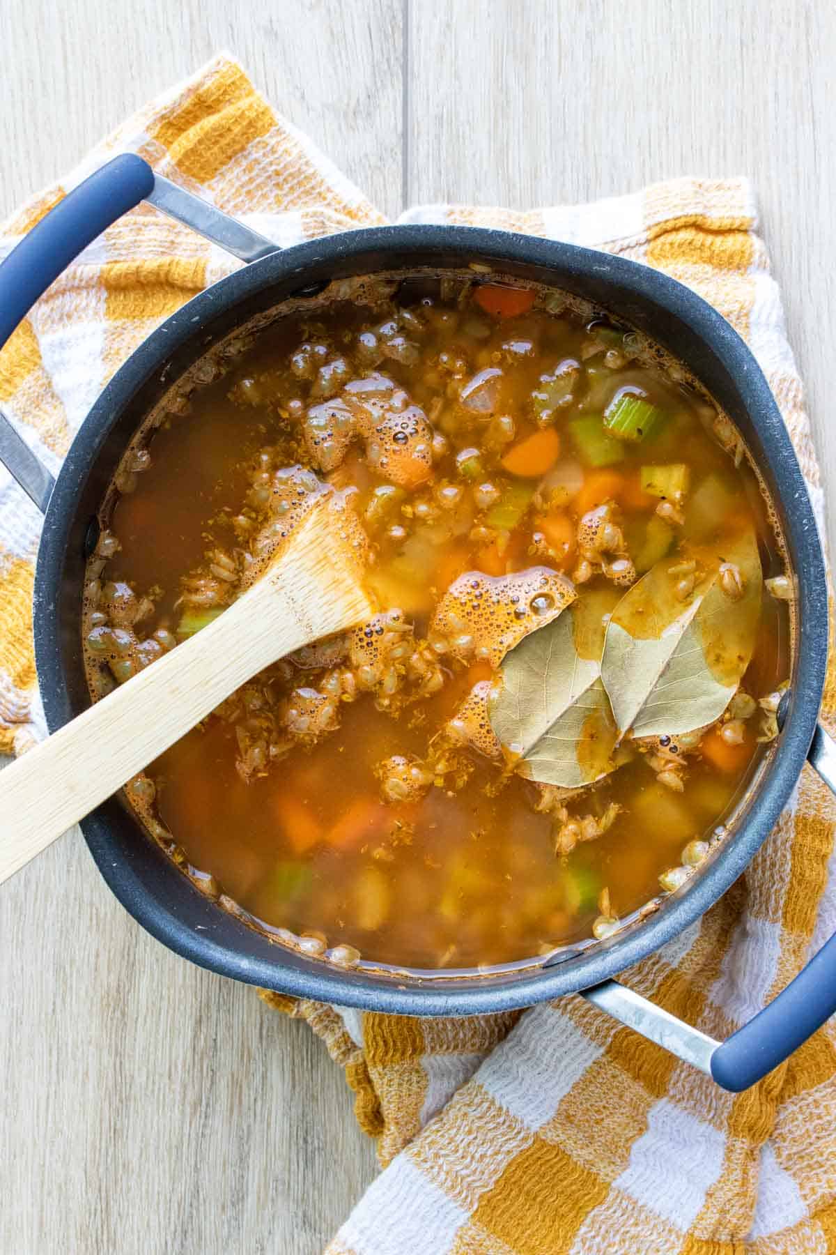 Wooden spoon stirring veggie lentil soup in a big pot