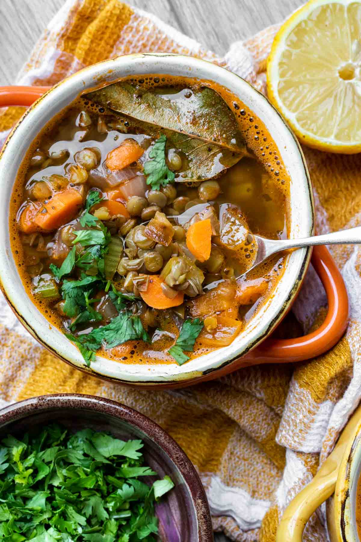 Close up of a spoon getting a bite of lentil soup with carrots from an orange bowl