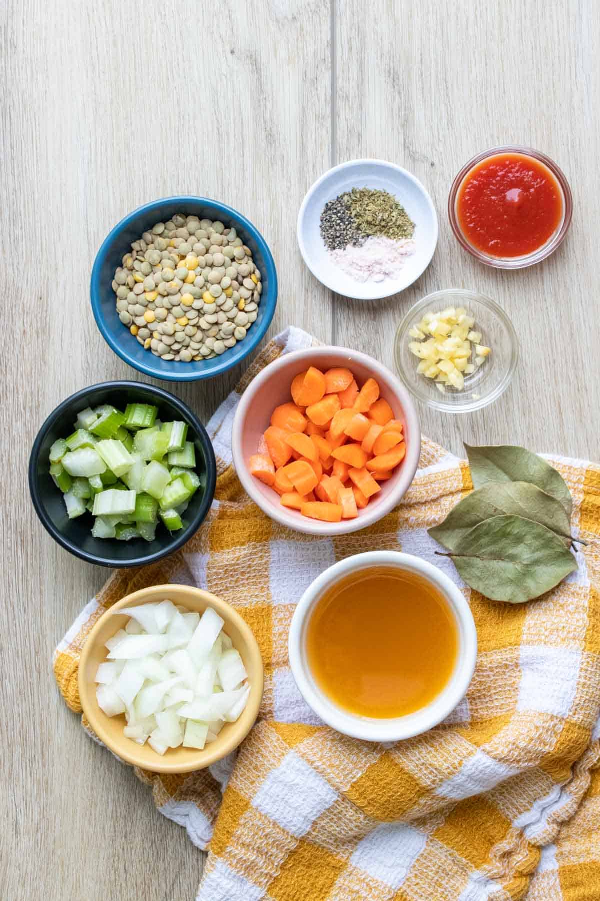 The ingredients needed for a veggie lentil soup in bowls on a yellow and white towel