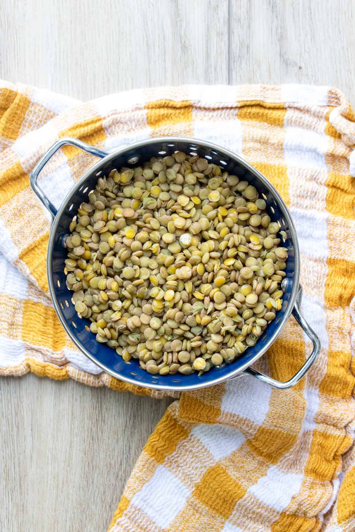 A blue colander filled with lentils on a yellow checkered towel