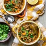 Two bowls of lentil soup with carrots and sprinkled with parsley and a bay leaf.