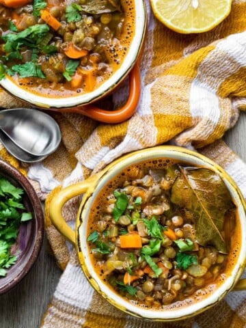 Two bowls of lentil soup with carrots and sprinkled with parsley and a bay leaf.