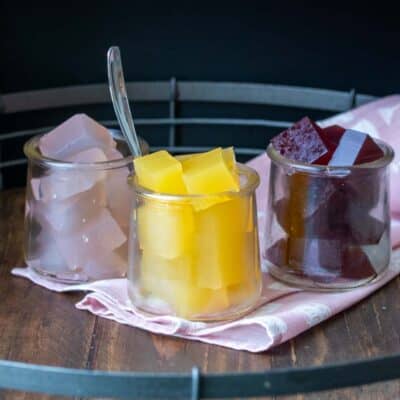 Different flavors of jello in three glass jars sitting on a pink napkin