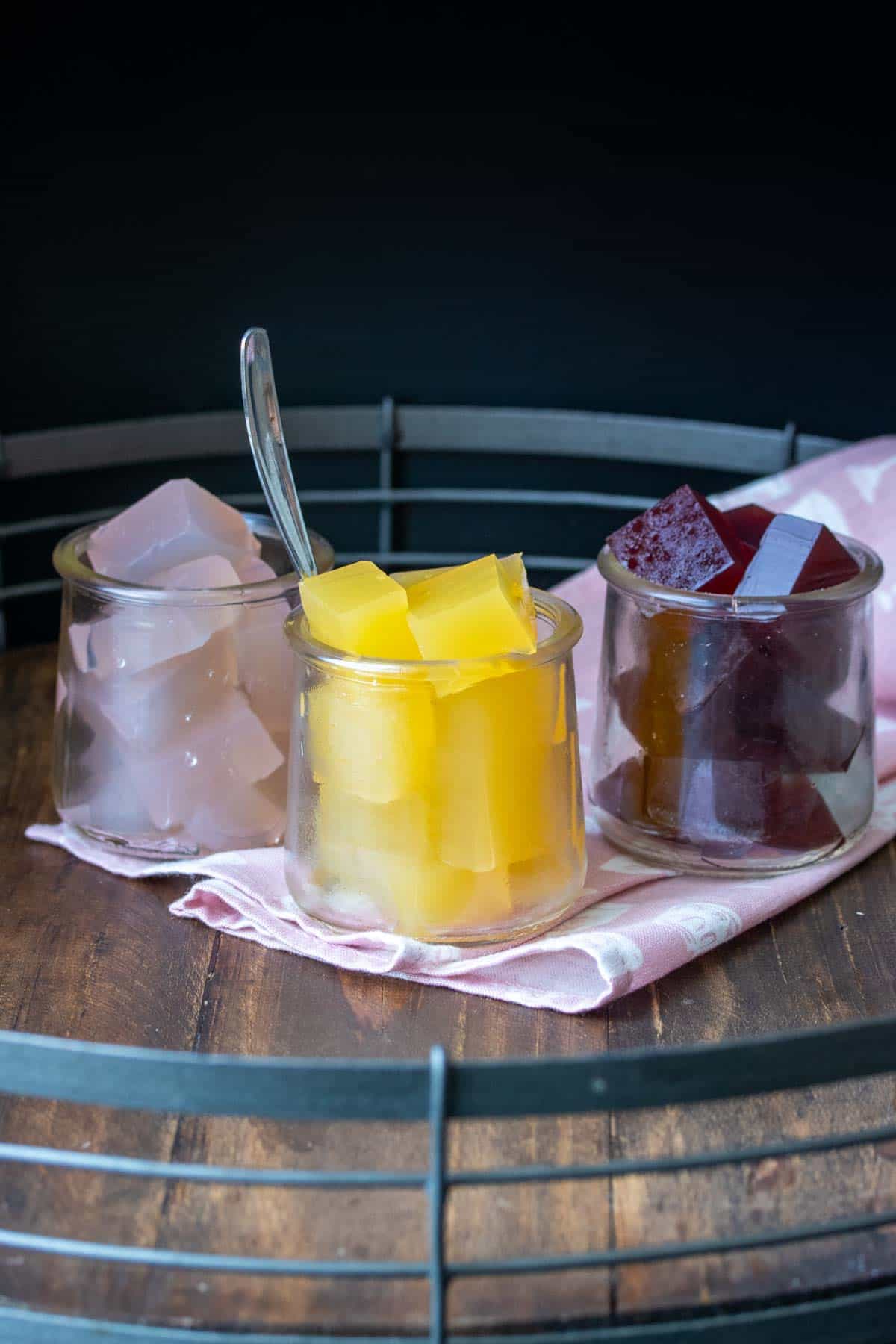 Different flavors of jello in three glass jars sitting on a pink napkin