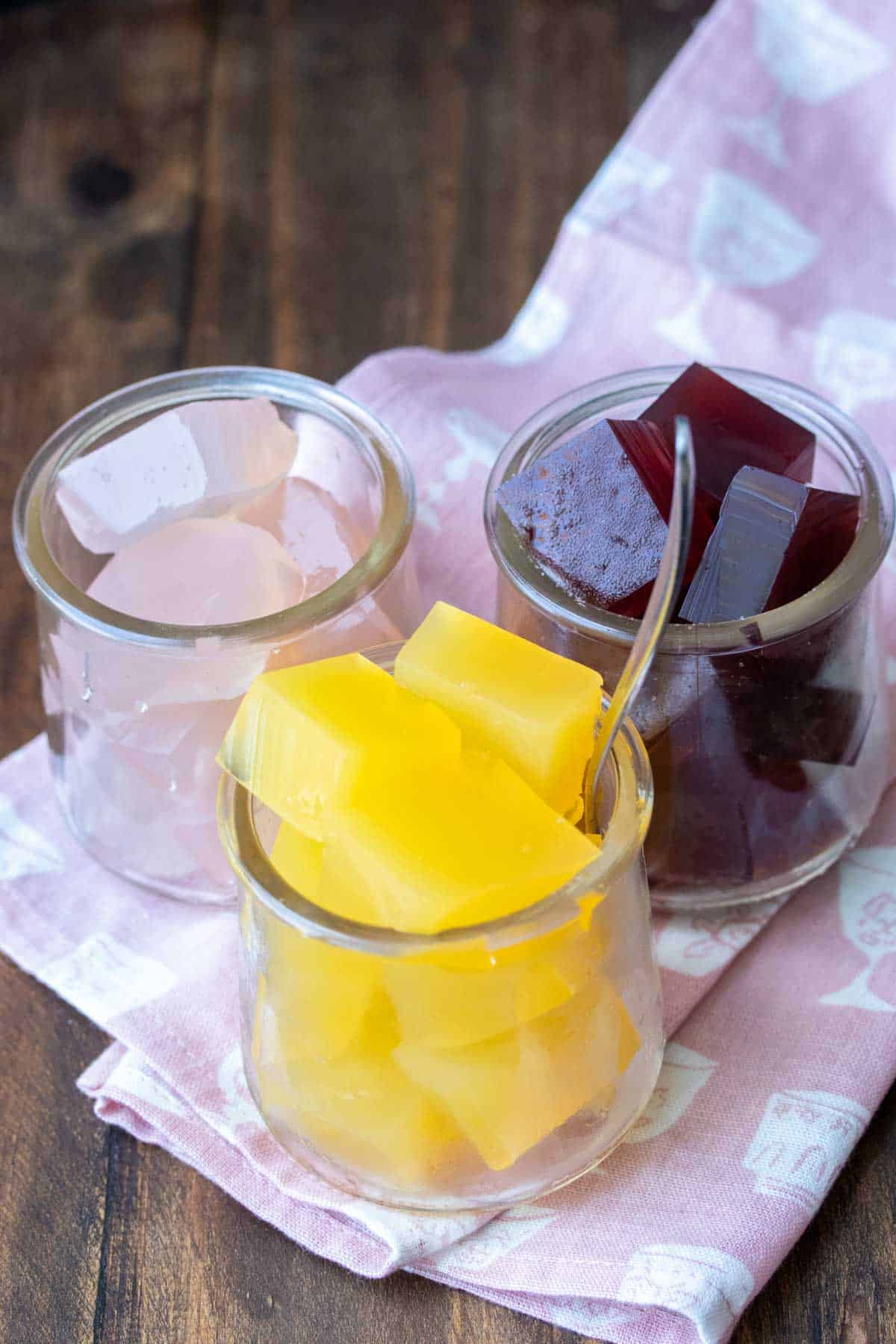 Three glass jars on a pink napkin filled with different flavors of jello