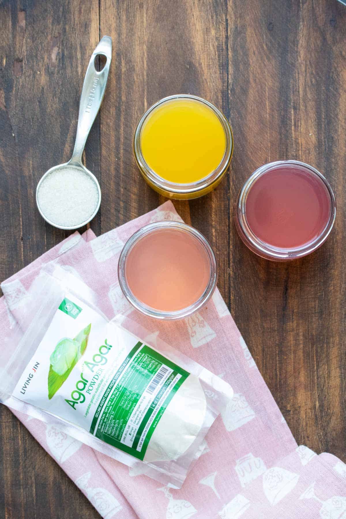 Top view of three jars of different colored liquids next to a tablespoon of powder and a plastic container bag