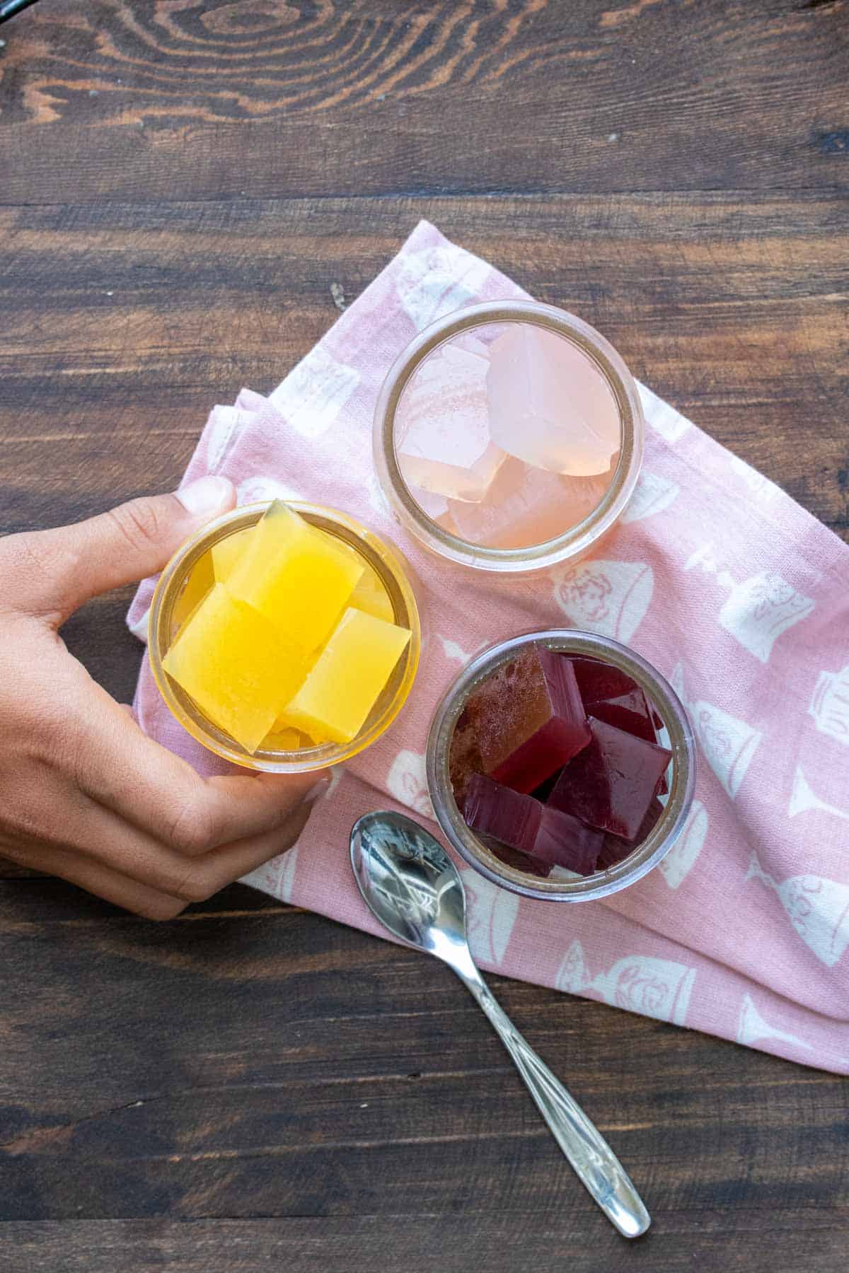 Three glass jars filled with different flavored jello cubes on a pink napkin