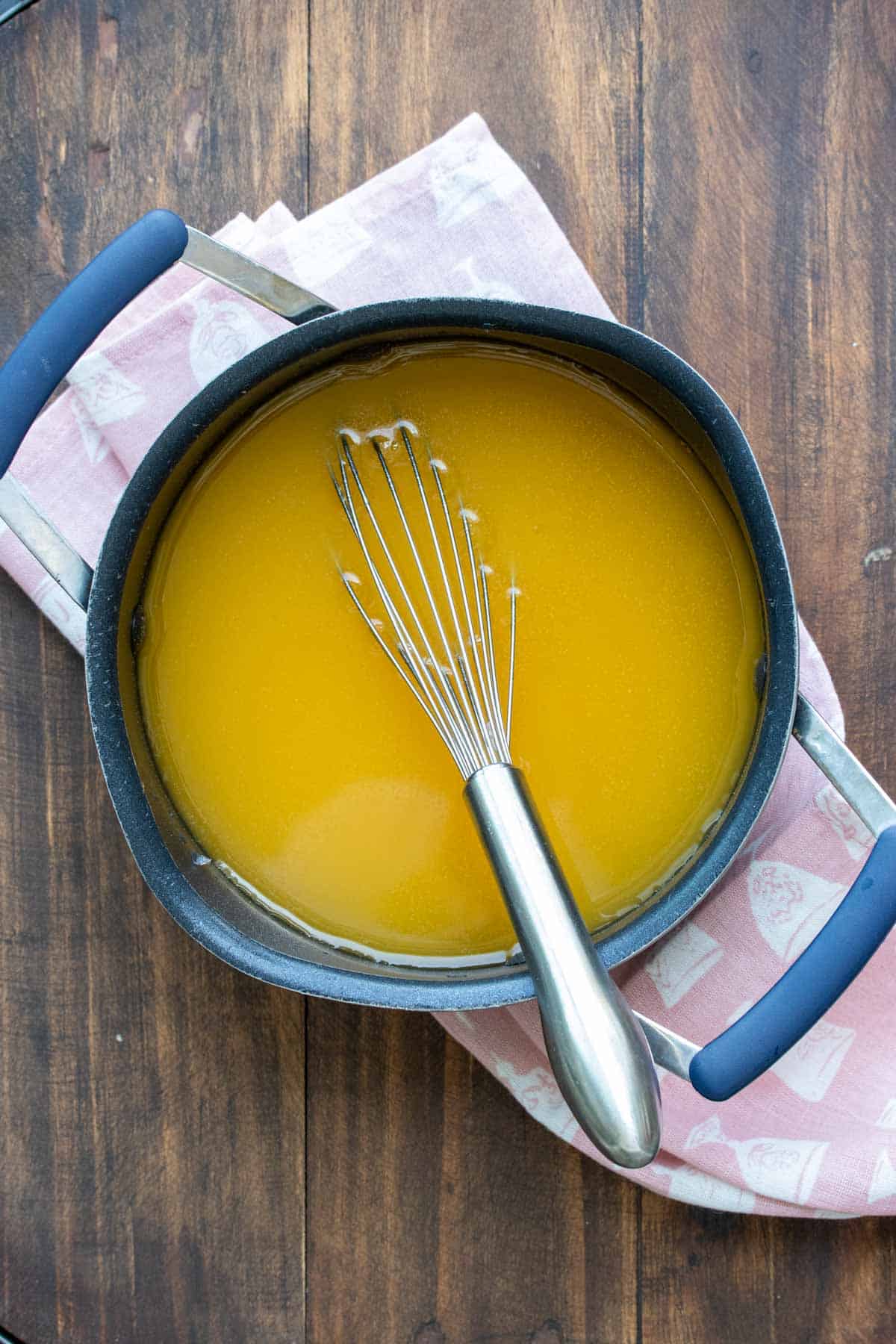 Whisk mixing an orange liquid in a black pot on a wooden surface