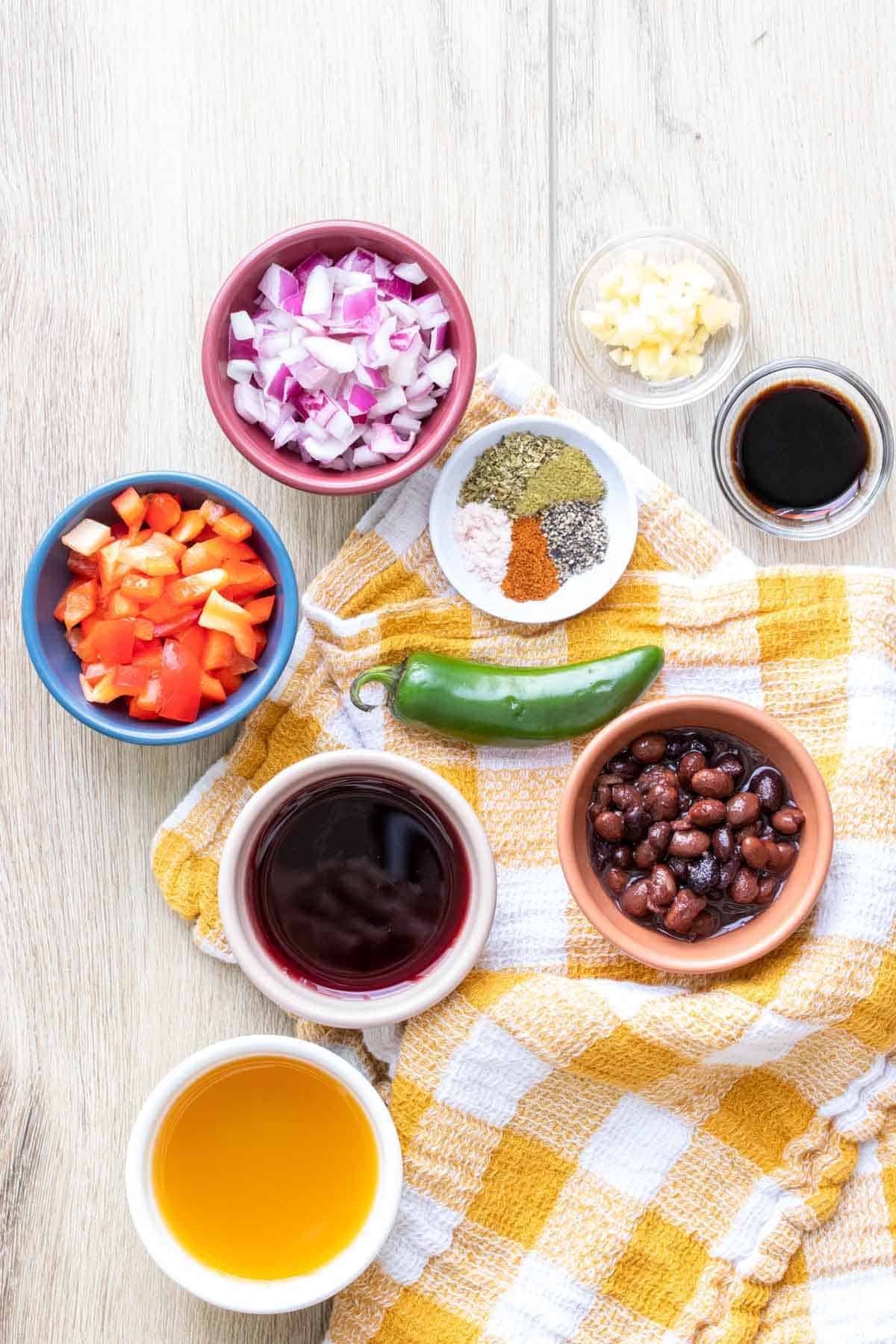 Ingredients to make black bean soup in colored bowls on a checkered towel