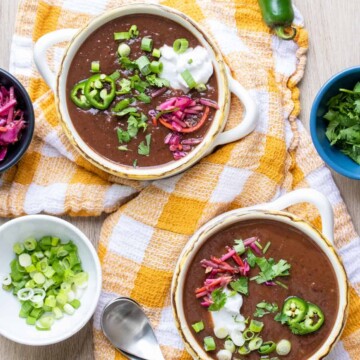 Two soup bowls on a checkered towel with black bean soup and surrounded by toppings